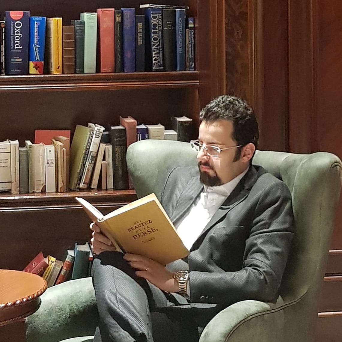 Dana Bina reading in a library armchair, preparing research for a keynote presentation