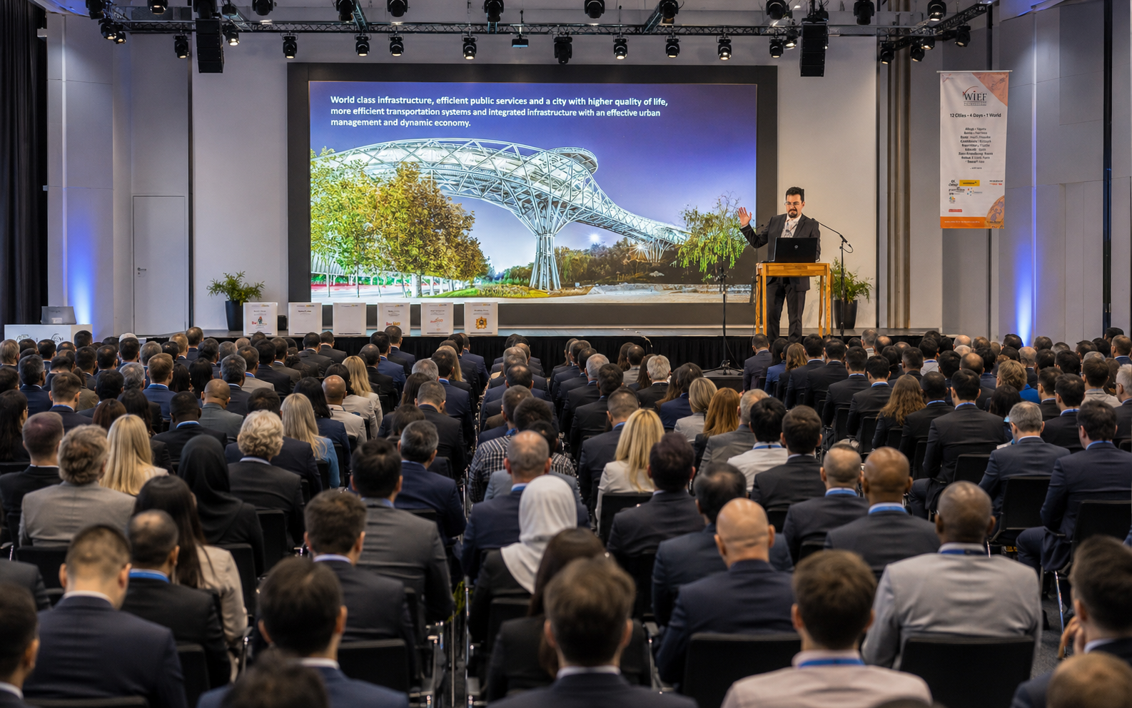 Dana Bina delivering a smart-city keynote to a full conference hall, presenting a slide on world-class infrastructure, efficient public services and integrated urban management